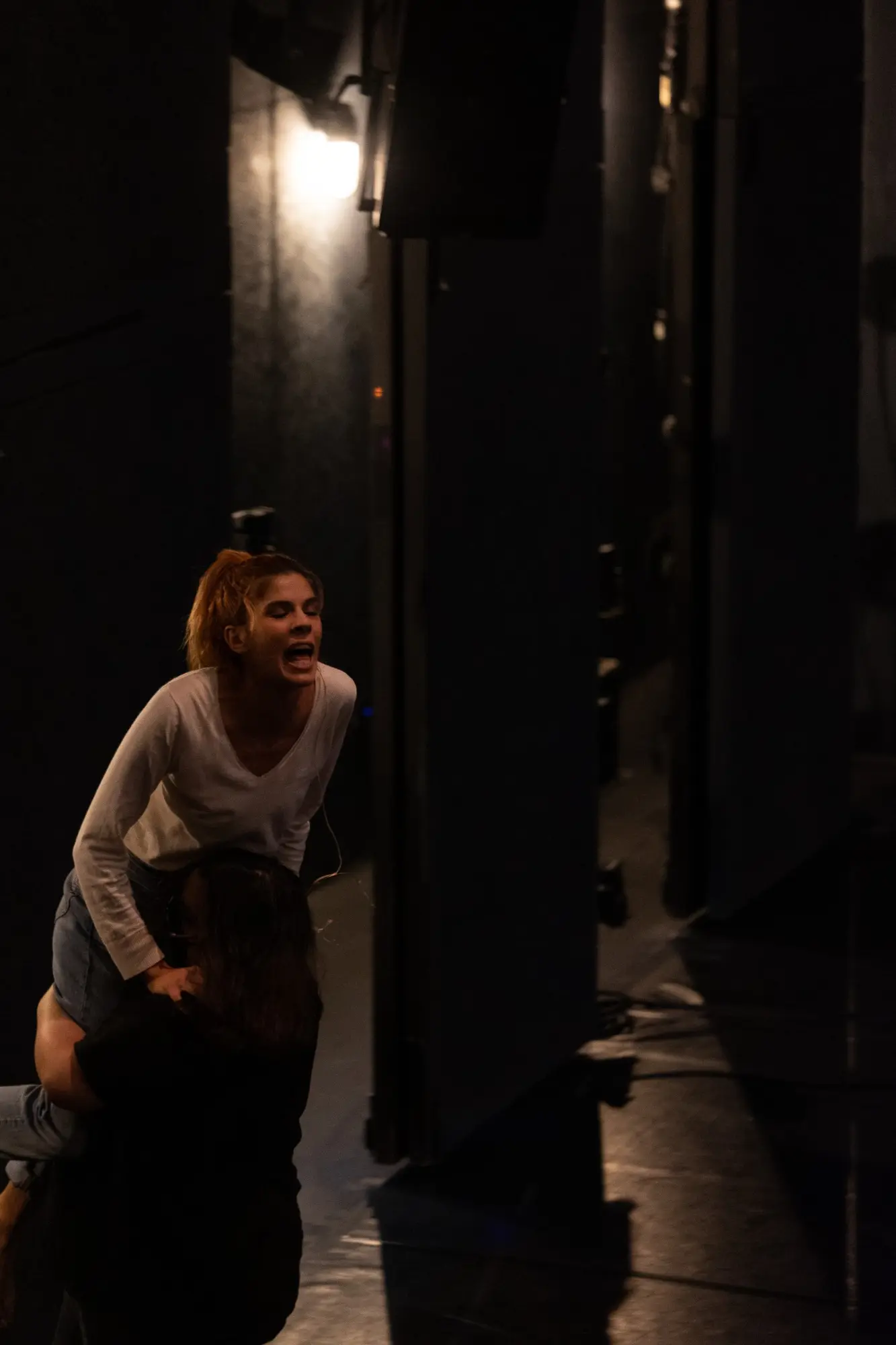 A performer advances through a narrow corridor of stage light