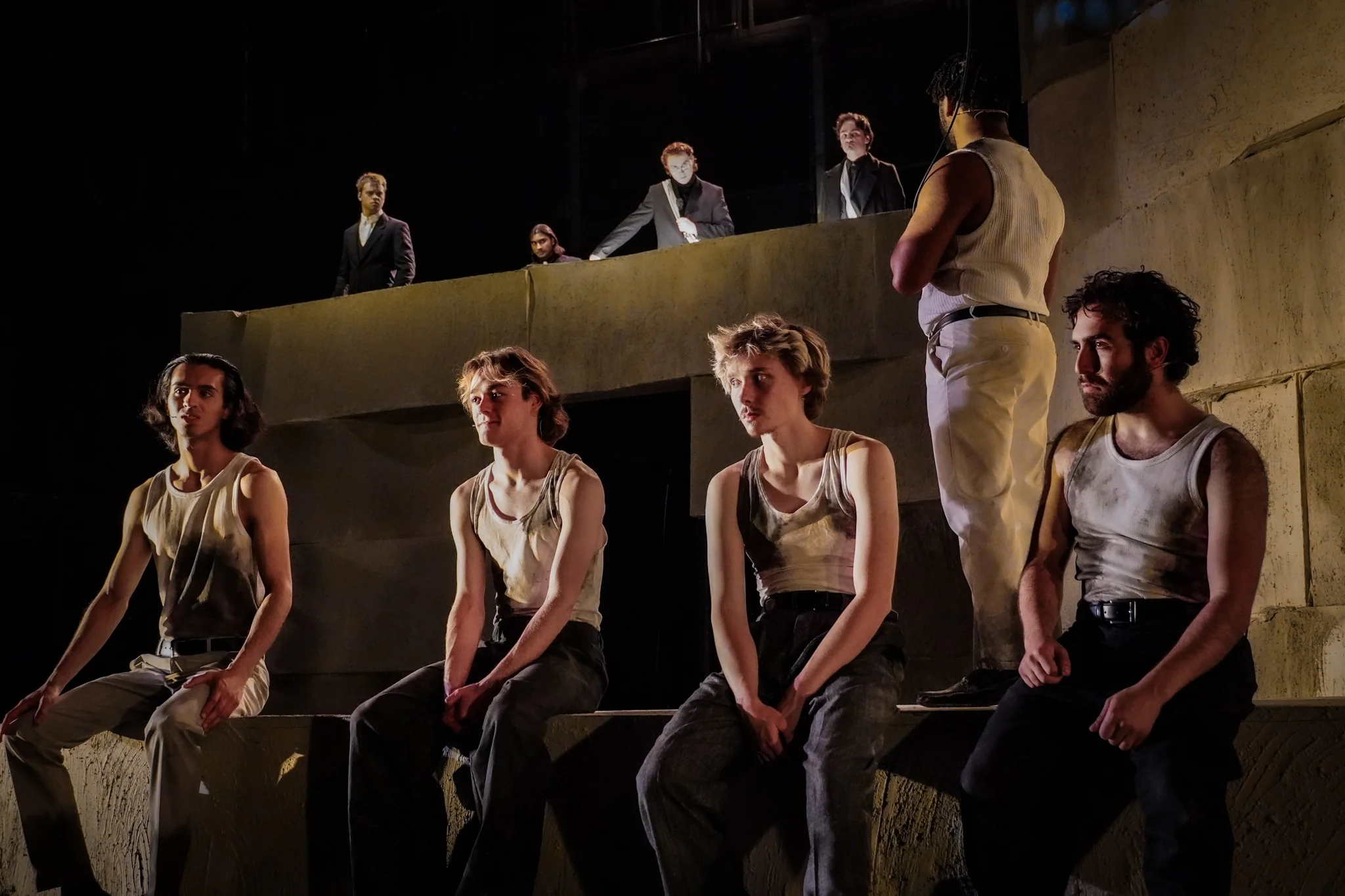 The ensemble sits and stands across the quarry set