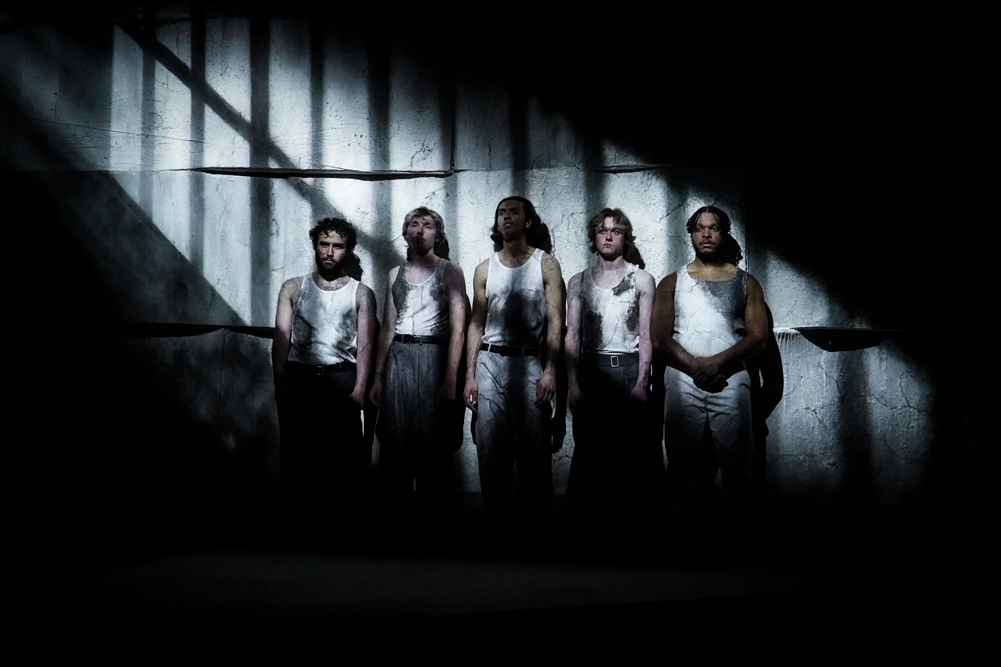 Five performers stand against a stark wall