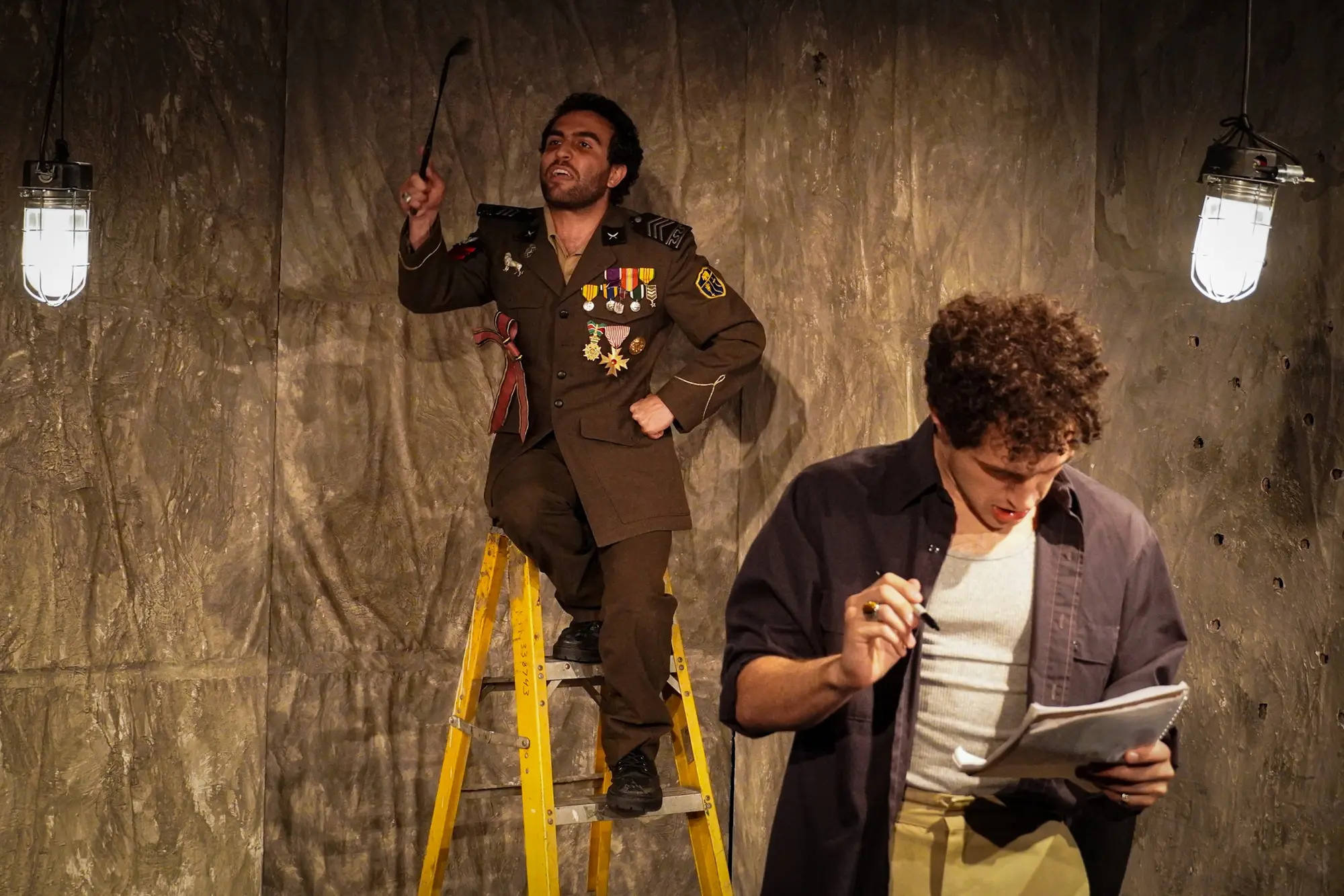 The general and servant perform beside a ladder and red telephone
