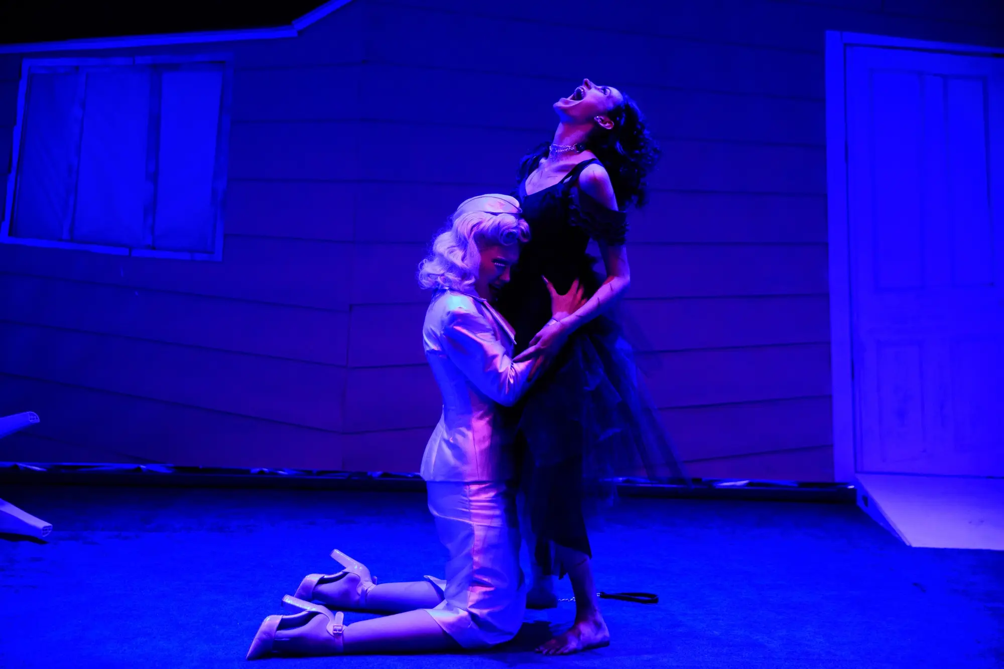 Two performers embrace in deep blue light