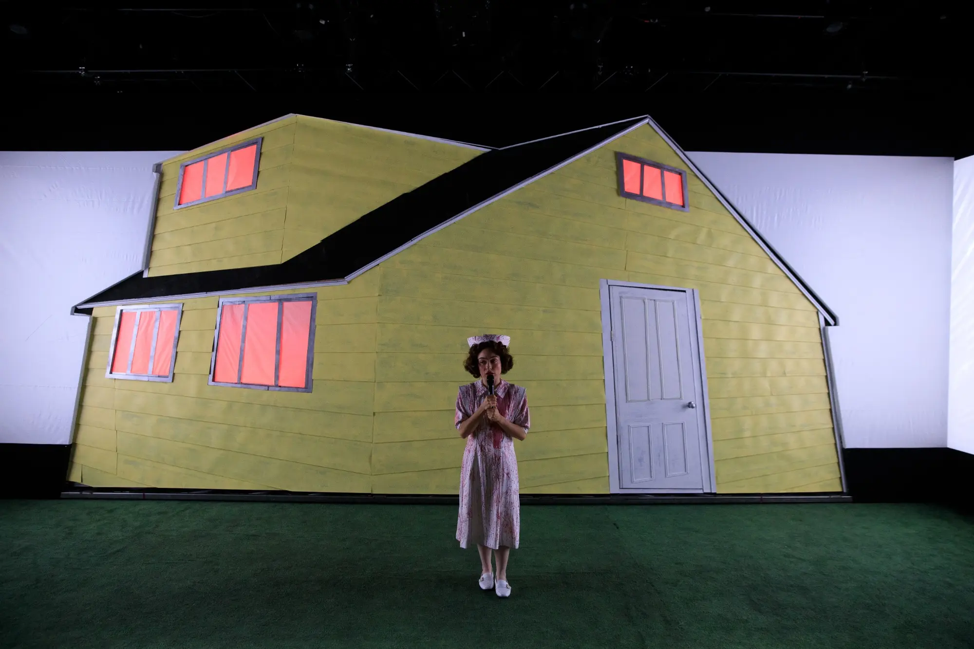 A lone woman stands before the yellow house