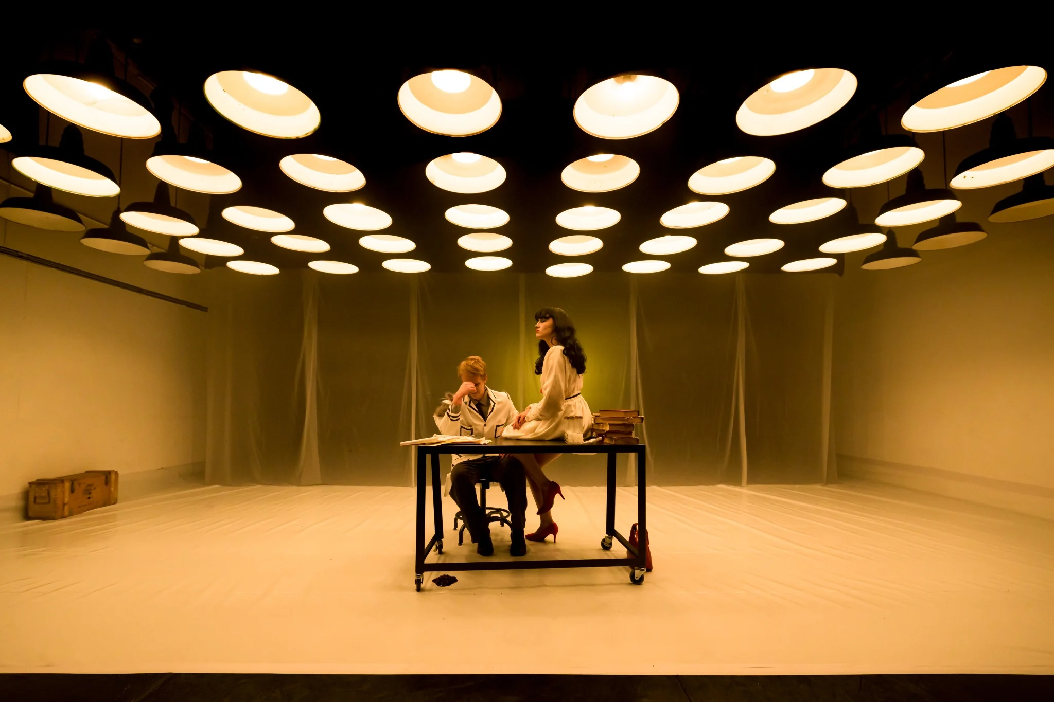 A woman sits on a laboratory table beside a scientist beneath rows of lights