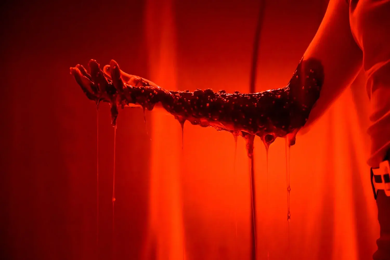 A viscous substance stretches between gloved hands under red light