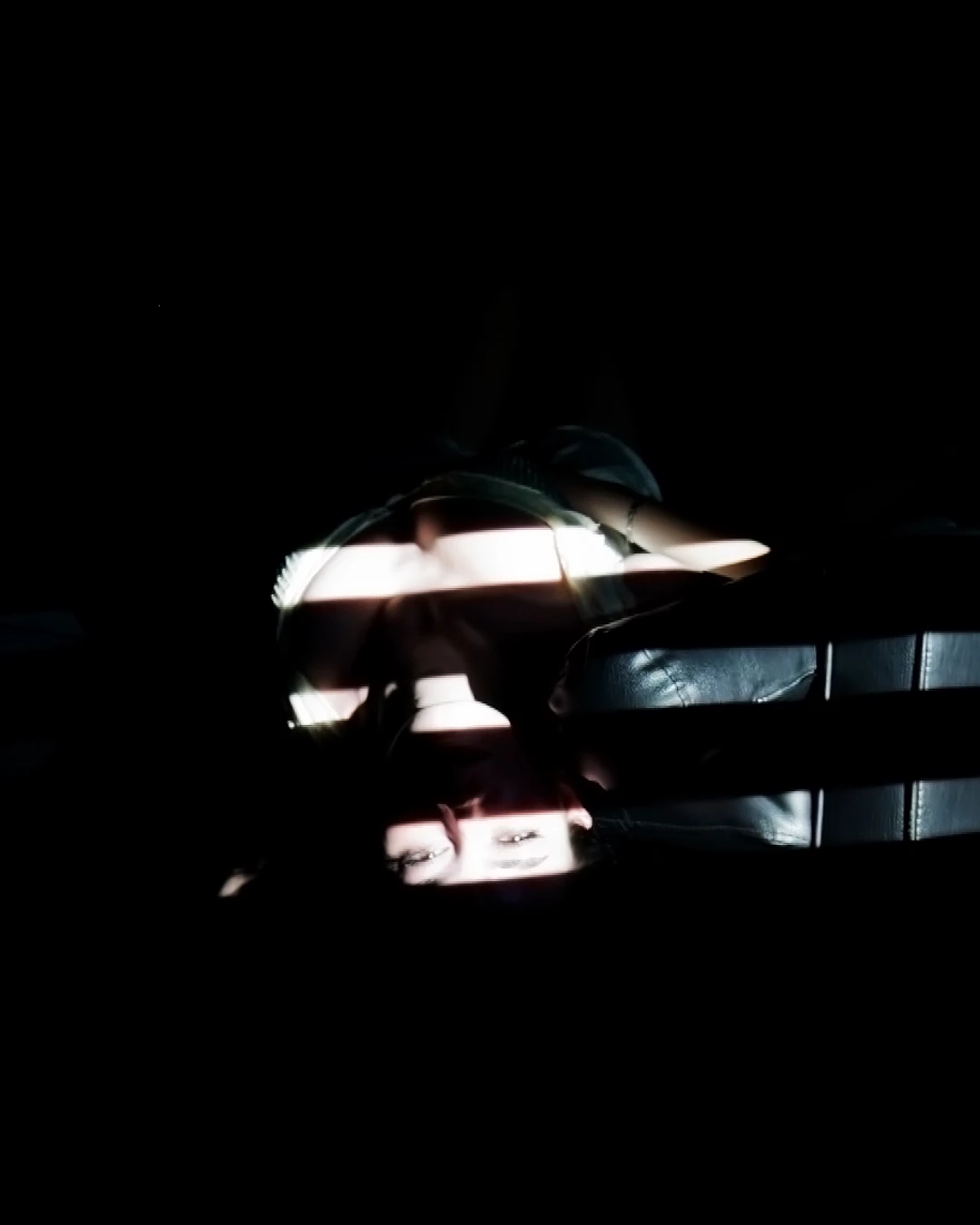 A reclining performer is crossed by bands of light